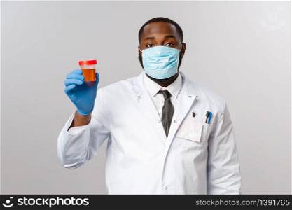 Covid19, pandemic and healthcare concept. African-american doctor in face-mask and latex gloves, study medical tests, got urinalysis from patient showing it, standing grey background.. Covid19, pandemic and healthcare concept. African-american doctor in face-mask and latex gloves, study medical tests, got urinalysis from patient showing it, standing grey background