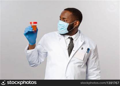 Covid19, pandemic and healthcare concept. Impressed and curious african-american doctor studying patient analysis, looking at urine test with intrigue, wear face mask and medical latex gloves.. Covid19, pandemic and healthcare concept. Impressed and curious african-american doctor studying patient analysis, looking at urine test with intrigue, wear face mask and medical latex gloves
