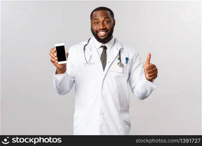 Covid19, pandemic and online appointment concept. Handsome smiling african-american doctor recommend use mobile app for treating patients, call physician and consult about treatment or consult.. Covid19, pandemic and online appointment concept. Handsome smiling african-american doctor recommend use mobile app for treating patients, call physician and consult about treatment or consult
