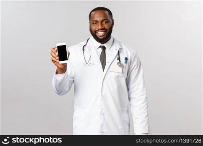 Covid19, pandemic and online appointment concept. Smiling professional, african american male doctor recommend staying at home and use mobile app receive treatment while social-distancing.. Covid19, pandemic and online appointment concept. Smiling professional, african american male doctor recommend staying at home and use mobile app receive treatment while social-distancing