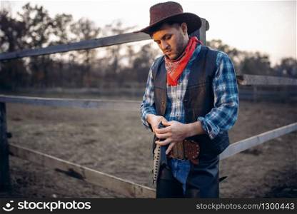 Cowboy checks his revolver before gunfight on ranch, western. Vintage male person with gun on farm, wild west adventure. Cowboy checks revolver before gunfight on ranch