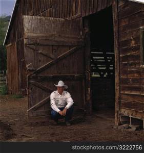Cowboy Crouching next to Barn