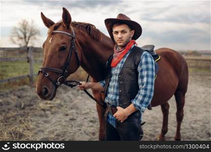 Cowboy in jeans and leather jacket poses with horse on texas farm, western. Vintage male person with animal, american culture