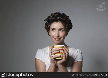 Coy young woman with hair curlers holding cup