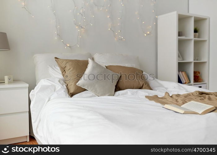 coziness, comfort, interior and holidays concept - cozy bedroom with bed and christmas garland lights at home