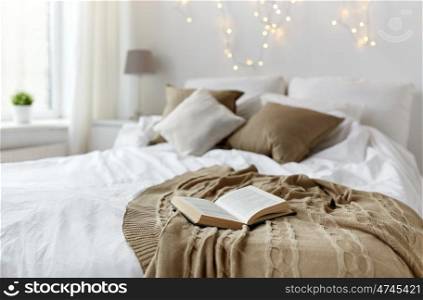 coziness, comfort, interior and holidays concept - cozy bedroom with bed and christmas garland lights at home. bedroom with bed and christmas garland at home