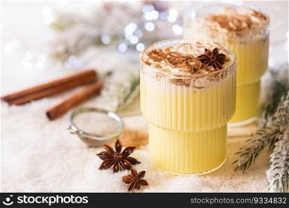Cozy atmosphere with glass of Eggnog, Christmas winter alcohol drink decorated by snow and christmas lights. Glass of Eggnog cocktail