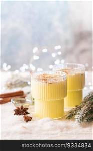 Cozy atmosphere with glass of Eggnog, Christmas winter alcohol drink decorated by snow and christmas lights. Glass of Eggnog cocktail