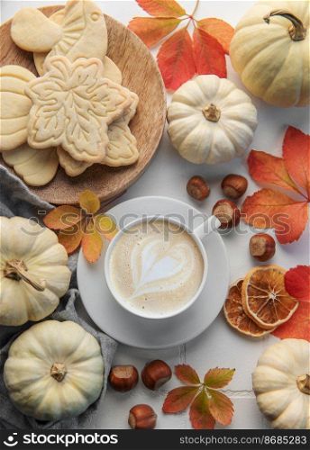 Cozy autumn composition. Hot coffee with cookies in a white cup  surrounded by autumn leaves and pumpkins on a white wooden background. 