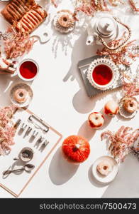 Cozy autumn home background with tea setting, cakes, autumn flowers and leaves, little pumpkins and clipping board with word autumn on white desk. Top view. Copy space. Frame