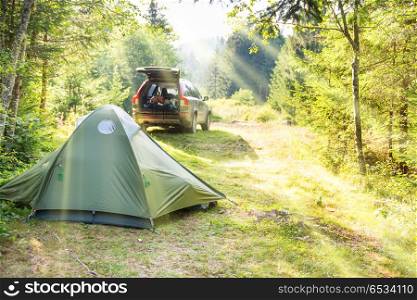 Cozy camping on green sunny lawn with tent and a car. Cozy camping with tent and a car