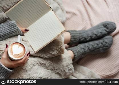 Cozy home, woman covered with warm blanket, drinks coffee and reeds the book.  Relax, carefree, comfort lifestyle.