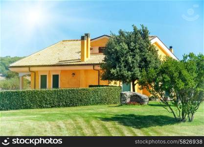 Cozy house with garden, trees and green lawn. Bright sun on the blue sky.