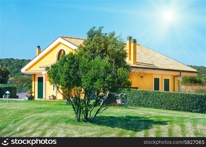Cozy house with garden, trees and green lawn. Bright sun on the blue sky.