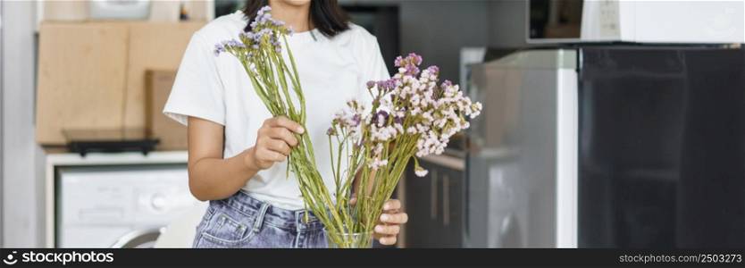 Cozy lifestyle concept, Young woman arrange flowers to decorate in vase on table in kitchen room.