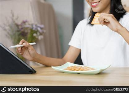 Cozy lifestyle concept, Young woman using tablet and eating crackers while leisure at home.