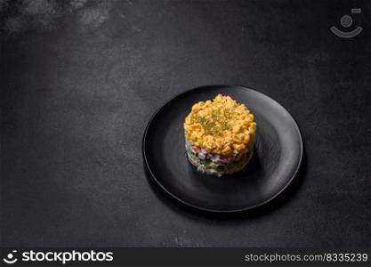 Crab salad with corn, laid out on a black plate for portion serving in a festive table setting. Fresh vegetable salad with corn, pepper, crab, cucumber, eggs and mayonnaise
