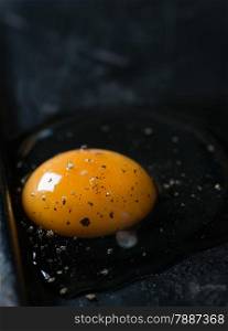 Cracked chicken egg with black pepper on dark background, selective focus