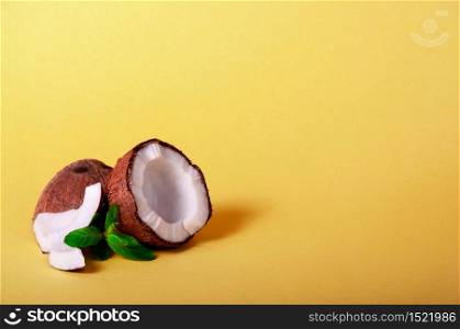 Cracked Coconut with Mint on Yellow Background. Exotic Food. Summer Tropical Concept. Copy Space For Your Text.. Cracked Coconut with Mint on Yellow Background. Exotic Food. Summer Tropical Concept. Copy Space For Your Text