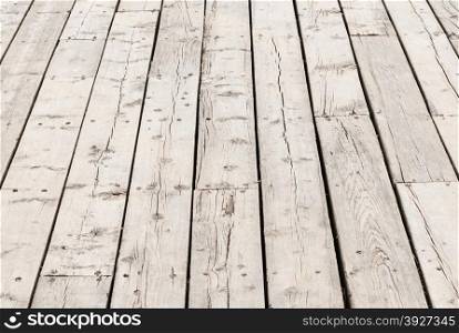 Cracked weathered gray wooden deck surface boards in perspective.