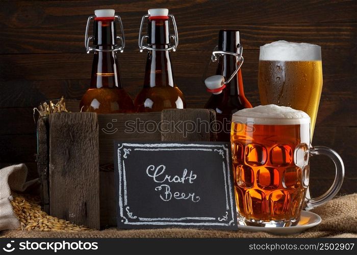 Craft beer glass and vintage wooden crate with beer bottles on burlap cloth with barley seeds