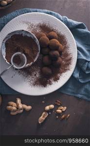 Craft chocolate truffles on plate with cocoa powder and peanuts.