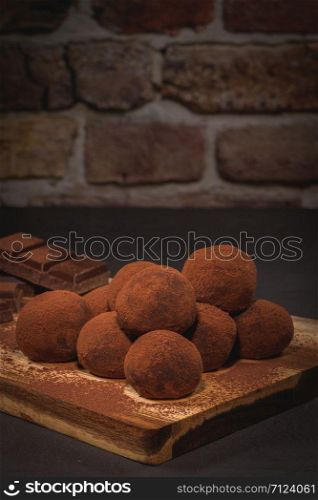 Craft chocolate truffles on wooden board with cocoa powder.