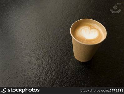 Craft cup of coffee with heart shape. Copy space on black textured table.. Craft cup of coffee with heart shape. Copy space on a black textured table.