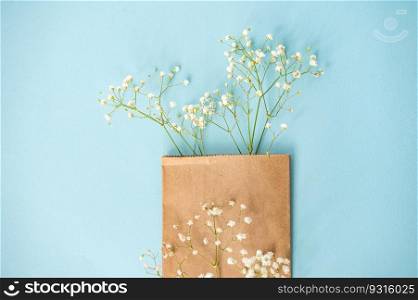 Craft package with gypsophila flowers on a bright blue background. View from above. Copy space. Creative flat desktop photo. Blue background with gypsophile on top with empty space for text
