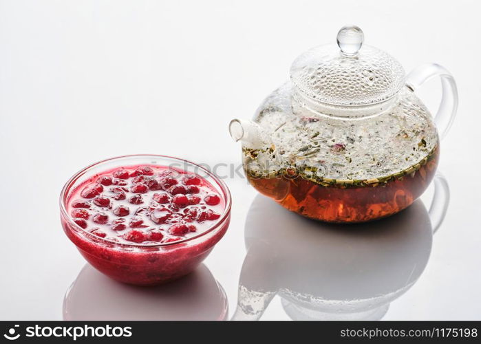 Cranberry jam in a glass bowl and teapot on a white background