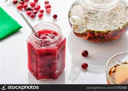 Cranberry jam in a glass jar and teapot on a white background