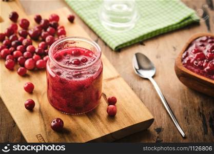 Cranberry jam in a glass jar on a wooden board