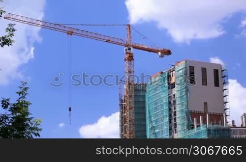 Crane and construction site against blue sky. Real time.