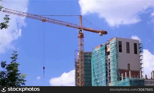 Crane and construction site against blue sky. Real time.