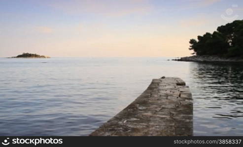 Crane shot. Coastline, water surface, causeway and a small island in the distance.