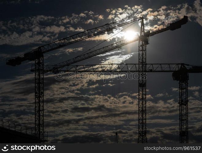 Cranes on a construction site with a cloudy sky during sundown