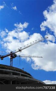 Cranes on construction site against blue sky and clouds.