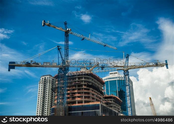 Cranes on modern skyscraper construction in city at sunny day with blue sky