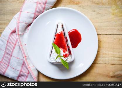 Crape cake slice with strawberry sauce on white plate on table wood background / Piece of cake rainbows with whipped cream top view