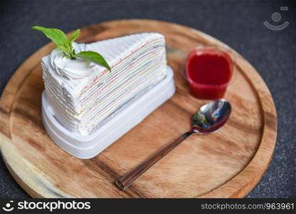 Crape cake slice with strawberry sauce on wooden plate spoon and dark background / Piece of cake rainbows with whipped cream