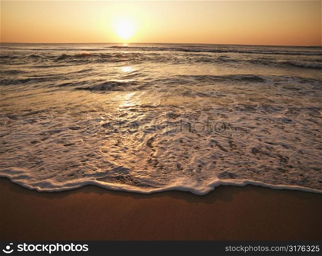 Crashing waves with sun setting on horizon in background.