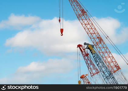 Crawler crane against blue sky and white clouds. Real estate industry. Red crawler crane use reel lift up equipment in construction site. Crane for rent. Crane dealership for construction business.