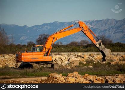 Crawler excavator clearing piles of rocks. Orange color machine