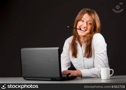 crazy business woman is sitting in the office with laptop and working hard with pencil in her teeth