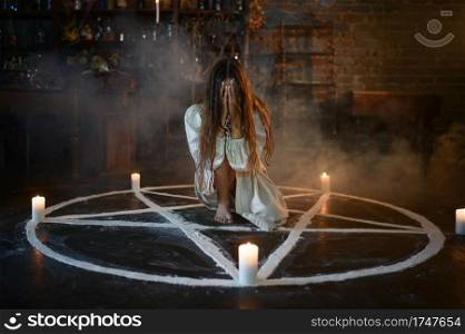 Crazy demonic woman sitting in magic circle with candles, demons casting out. Exorcism, mystery paranormal ritual, dark religion, night horror, potions on shelf on background. Crazy woman sitting in magic circle with candles