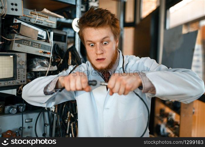 Crazy engineer connects wires under tension in laboratory. Electrical testing tools on background. Lab equipment, engineering workshop. Engineer connects wires under tension in lab