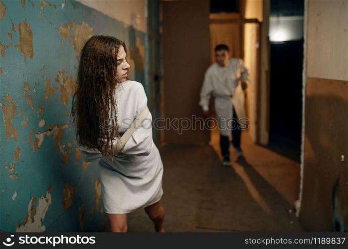 Crazy female patient in straitjacket runs away from the psychiatrist, mental hospital. Woman in strait jacket undergoing treatment in clinic for the mentally ill