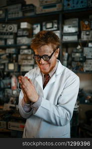 Crazy male scientist in glasses conducts a test in laboratory. Electrical testing tools on background. Lab equipment, engineering workshop