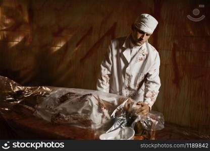 Crazy psychiatrist maniac looks at female patient&rsquo;s body, experiment in mental hospital basement, bloody walls on background. Victim of mad doctor in clinic for the mentally ill. Psychiatrist maniac looks at female patient&rsquo;s body
