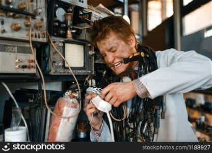Crazy scientist conducting an experiment in laboratory. Electrical testing tools on background. Lab equipment, engineering workshop. Crazy scientist conducting an experiment in lab